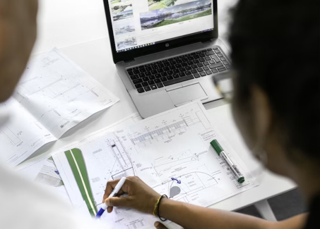 Two people standing and talking over a set of blueprints.