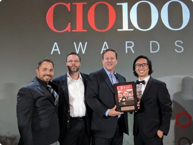 A group of four people holding an award that are standing in front of a wall displaying a CIO100 awards logo.
