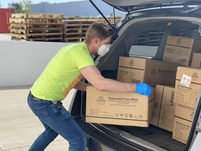 Person standing at the back of a vehicle loading boxes into the trunk.