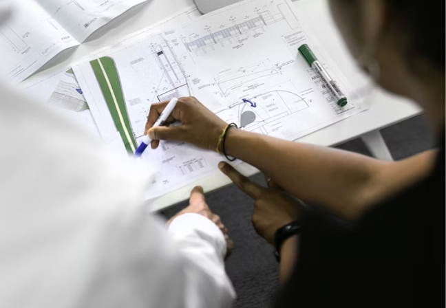 Two people standing and talking over a set of blueprints.