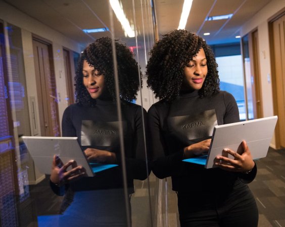 A woman with a computer in her hands leaning against a glass wall.