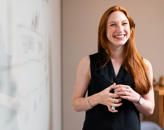 A smiling woman standing next to a whiteboard.